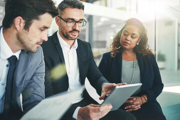 Comparing their figures. Shot of a group of coworkers talking together over a digital tablet in an...