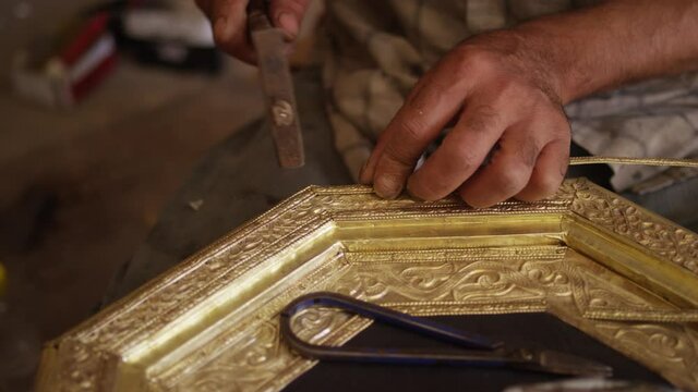 Close up of artisan hands working on a gold metal frame in smith shop in Morocco