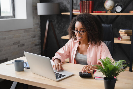Young african student worker businesswoman freelancer counting funds domestic bills on calculator while using laptop for e-banking, paperwork, debt and loan