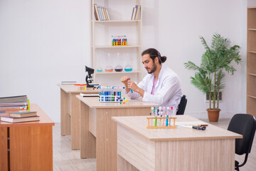 Young male chemist sitting at the desk in the classroom