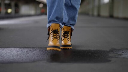 woman in trendy yellow shoes and blue jeans is walking railway station platform, closeup of feet