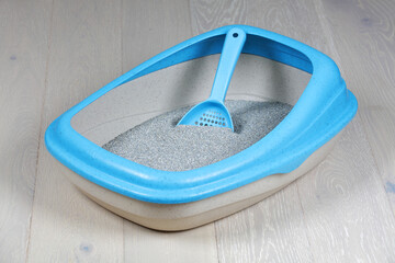 Cat litter tray and scoop on a wood floor