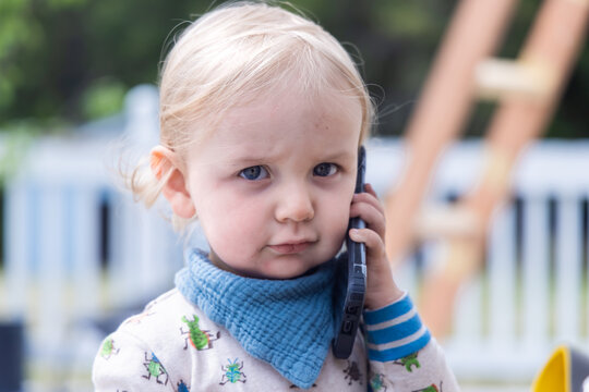 Portrait of a young caucasian toddler holding a smartphone to his ear. Playing and learning communication with soft blurry background and copy space.