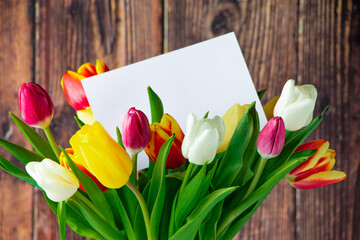 Colorful tulips bouquet and greeting card on wooden background. Holiday gift.