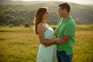 Young husband and his pregnant wife in the summer field