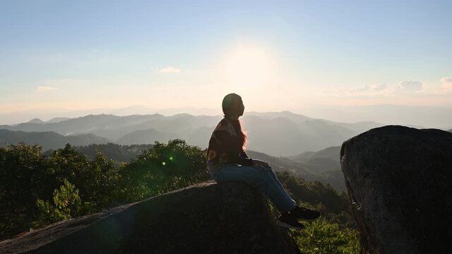 Young asian woman relaxing on rock of mountain peak in national park on summertime at sunset