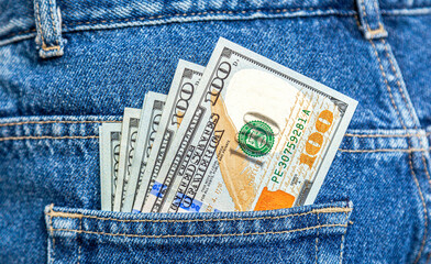 Banknotes of American dollars sticking out of the blue jeans pocket