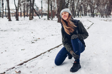 Runner injured leg during training in snowy winter park. Woman feels ankle pain holding it with hand. Exercises outdoors