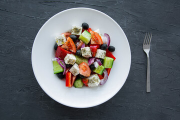 Tasty greek salad with fresh vegetables on black stone background, top view. 