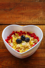 Puff salad with chicken breast and pineapple, garnished with pomegranate and olives in a heart salad bowl on a wooden table.
