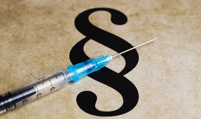 Closeup of paragraph symbol with vaccination injection syringe - mandatory vaccination concept 
