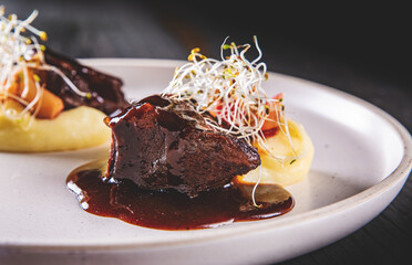 Stewed veal cheeks with mashed potatoes on plate on wooden table dark background