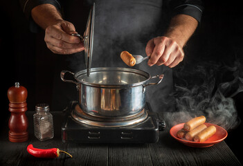 The chef cooks Vienna sausage in saucepan. Working environment in the restaurant kitchen. Delicious breakfast or dinner.