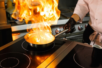  Close-up of the chef's hands cooking food on fire. The chef burns food in a professional kitchen.