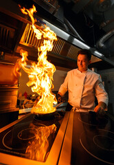  Close-up of the chef's hands cooking food on fire. The chef burns food in a professional kitchen.
