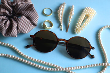 Tortoiseshell sunglasses, pearl necklace and hair barrettes, gold rings and scrunchie on bright...