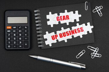 On the table is a calculator, a pen and a notebook with the inscription - Gear Up Business