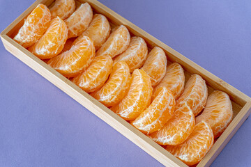 Tangerine segments in a square wooden bowl on a blue background.