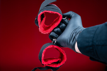 hands in black gloves holding handcuffs with red belts for bdsm sex games