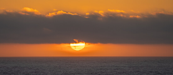 Sunset with alarge sun partially obscurred with clouds on the Oregon coast at Seaside