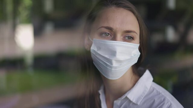 Close-up Portrait Of Caucasian Sad Woman In Covid-19 Face Mask Looking Out The Window Thinking. Lonely Frustrated Depressed Beautiful Lady Alone On Coronavirus Pandemic. Lockdown Isolation