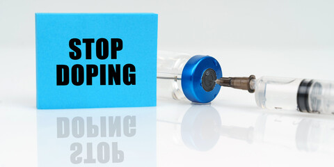 On a white reflective surface are a syringe, an injection and a blue plaque that says - Stop Doping