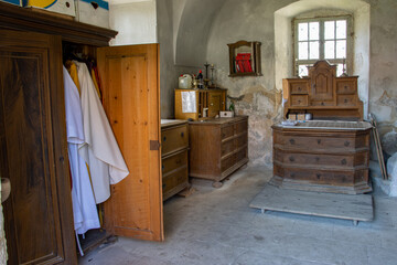 The sacristy of a country church with a old furniture and The vestments in an open cabinet.