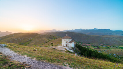 Fototapeta na wymiar The small octagonal chapel near Rocca Calascio castle ruins at sunset in backlight, landmark in the Gran Sasso National Park, Abruzzo, Italy. Mountains scenic background.