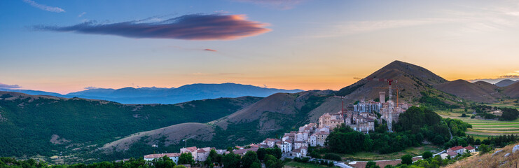Fototapeta na wymiar Sunset over medieval village perched on hill top, Santo Stefano di Sessanio, Abruzzo, Italy. Romantic sky and clouds above mountains landscape, tourism destination.