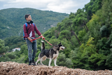 Handsome hiker boy with Siberian husky dog looking at beautiful view in mountains
