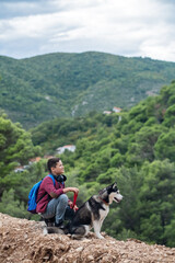 Handsome hiker boy with Siberian husky dog looking at beautiful view in mountains