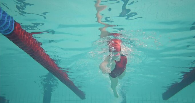 Portrait, woman swimmer trains in the pool, swims underwater. Woman swimmer works out the crawl style, bubbles under water. Preparing for the competition in the pool. 4k, ProRes