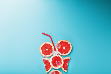 Grapefruit slices and ice cubes with a straw on a blue background in the shape of a cocktail.