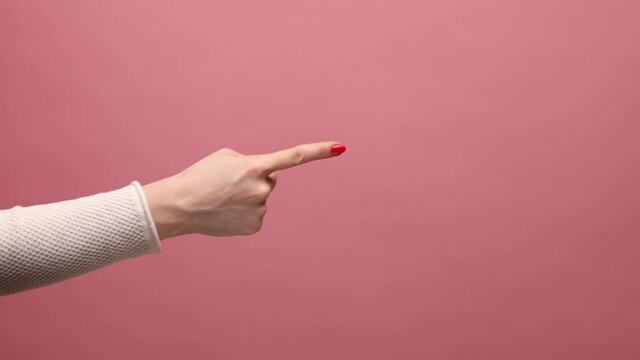 Profile side view closeup of woman hand pointing to someting with index finger, showing copyspace for advertising area. Indoor studio shot isolated on pink background.