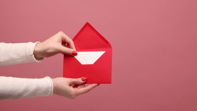 Profile side view closeup of woman hand holding dargging out red opened letter envelope, opening greeting card for holiday. Indoor studio shot isolated on pink background.