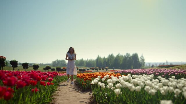 Beautiful woman with camera in tulips garden. Positive girl taking photopictures