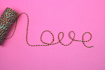 Red and white string making the word love on a pink background