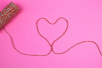 Red and white string making the shape of a heart on a pink background