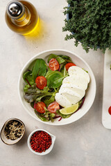 Salad with green leaves, lettuce, spinach, cherry tomatoes, mozzarella, olive oil, chilli pepper, lime juice on grey stone surface, top view