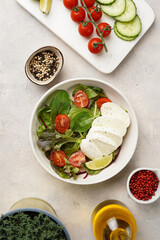 Salad with green leaves, lettuce, spinach, cherry tomatoes, mozzarella, olive oil, chilli pepper, lime juice on grey stone surface, top view