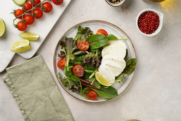 Salad with green leaves, lettuce, spinach, cherry tomatoes, mozzarella, olive oil, chilli pepper, lime juice on grey stone surface, top view