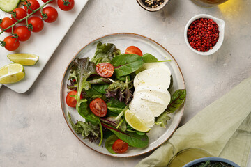 Salad with green leaves, lettuce, spinach, cherry tomatoes, mozzarella, olive oil, chilli pepper, lime juice on grey stone surface, top view