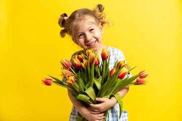 a small blonde on a yellow background with a bouquet of red tulips in her hands, laughing. holiday concept