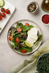 Salad with green leaves, lettuce, spinach, cherry tomatoes, mozzarella, olive oil, chilli pepper, lime juice on grey stone surface, top view