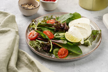 Salad with green leaves, lettuce, spinach, cherry tomatoes, mozzarella, olive oil, chilli pepper, lime juice on grey stone surface