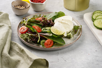 Salad with green leaves, lettuce, spinach, cherry tomatoes, mozzarella, olive oil, chilli pepper, lime juice on grey stone surface