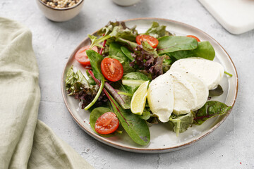 Salad with green leaves, lettuce, spinach, cherry tomatoes, mozzarella, olive oil, chilli pepper, lime juice on grey stone surface