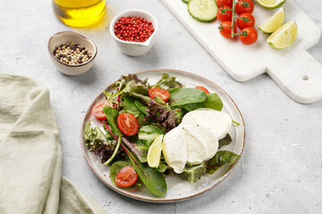 Salad with green leaves, lettuce, spinach, cherry tomatoes, mozzarella, olive oil, chilli pepper, lime juice on grey stone surface
