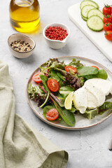 Salad with green leaves, lettuce, spinach, cherry tomatoes, mozzarella, olive oil, chilli pepper, lime juice on grey stone surface