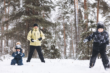 Father and sons having fun snowball fight together in winter forest. Happy children playing in snow...